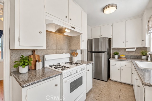 A clean, bright kitchen with white cabinetry, stainless steel refrigerator, white gas stove, and speckled laminate countertops.