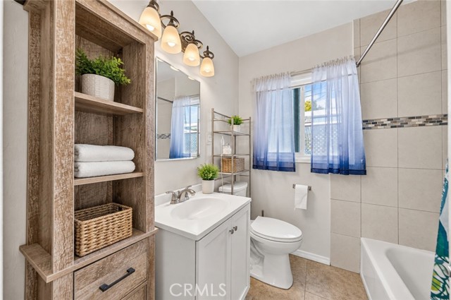 Modern bathroom with vanity, wood storage unit, toilet, and shower-tub combo