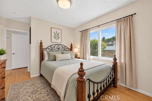A tidy, furnished bedroom with light walls, wood-tone flooring, and a queen-sized bed with a wooden and metal frame