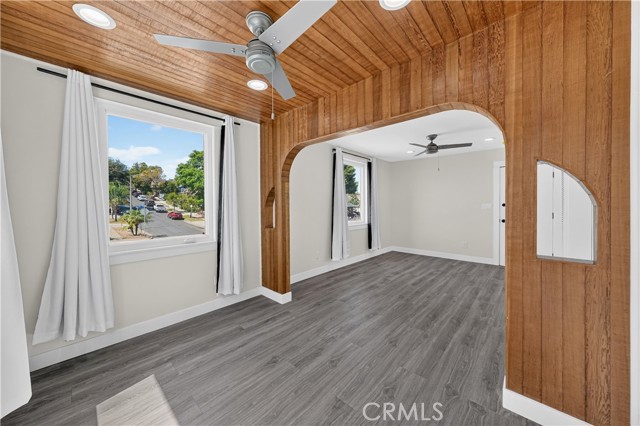 A living room with wood-paneled ceiling, wood-trimmed archway, gray laminate floors, and a ceiling fan.