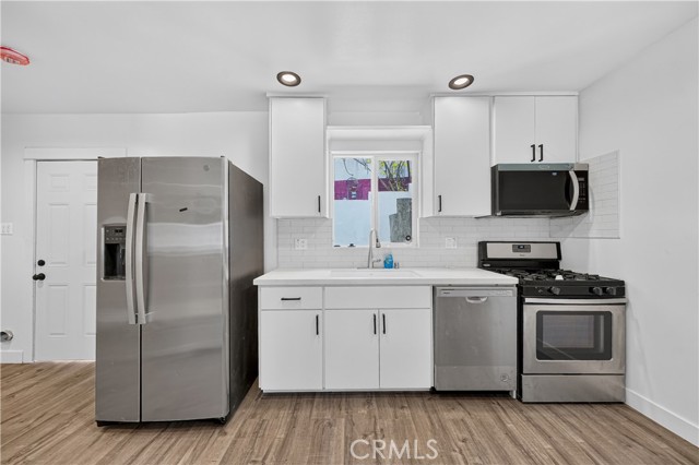 A modern kitchen with white cabinets, stainless steel appliances, and wood-look flooring.