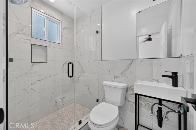 Modern bathroom with white marble-look tiles, walk-in glass shower, and a minimalist pedestal sink
