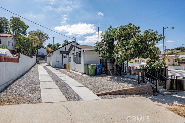 Exterior view of a small residential structure with a gravel driveway and a paved pathway leading to a side entrance.