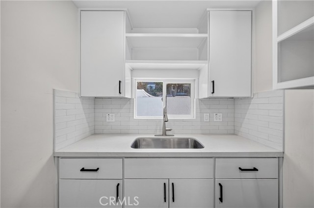 A modern kitchen sink area featuring white shaker cabinets, white subway tile backsplash, and dark hardware.