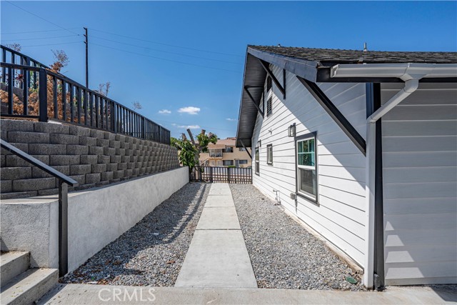 A narrow side yard walkway with gravel and a concrete path alongside a white exterior wall.