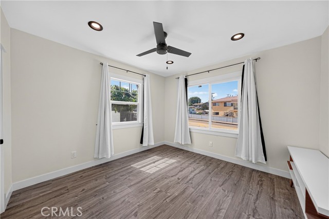 Spacious bedroom with grey wood-look vinyl plank flooring, neutral walls, white curtains, ceiling fan, and recessed lighting.