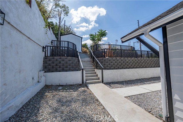 Concrete stairs leading up to a terraced backyard with gravel landscaping and a storage shed