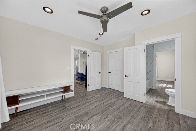 A bedroom featuring white walls, wood-look flooring, a modern ceiling fan, and access to an adjoining bathroom.