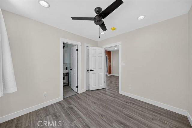 An empty bedroom with gray laminate floors, beige walls, a black ceiling fan, and doors leading to a bathroom and another area.