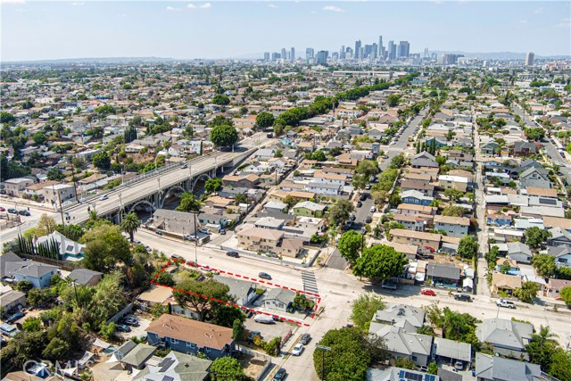 Aerial photograph highlighting a corner real estate property lot with a red outline in a dense residential neighborhood featuring a nearby highway bridge and a distant downtown Los Angeles city skyline.