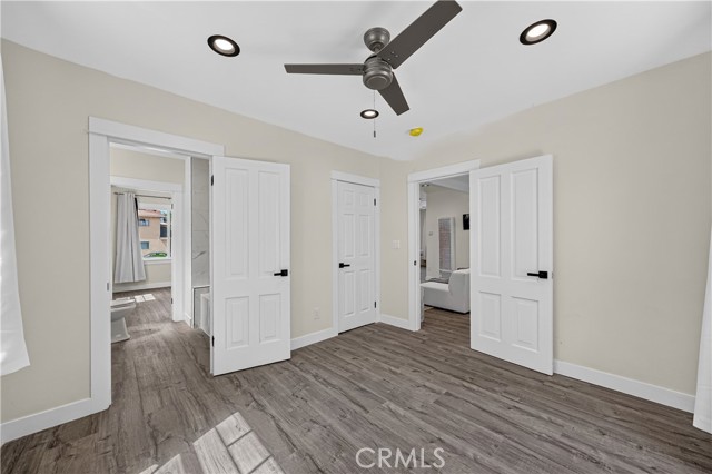 A bedroom with grey wood-look flooring, white walls, and multiple door openings showing adjacent rooms.