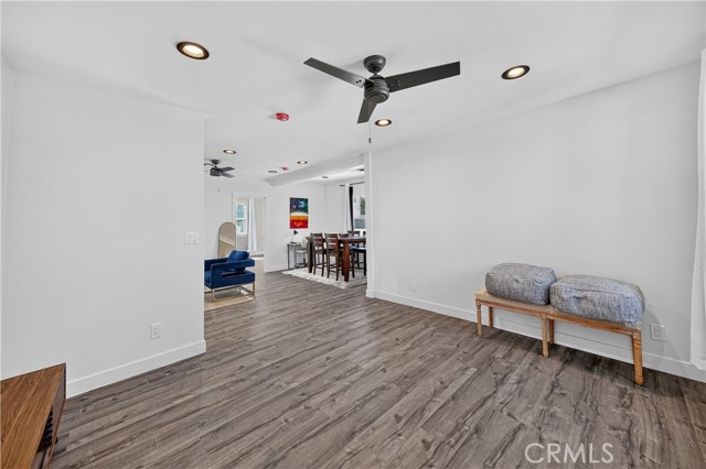 A wide angle shot of an open floor plan living room with wood-look laminate flooring, a ceiling fan, and a view into the dining area.