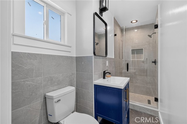 A modern bathroom with blue vanity, gray wall tile, and glass shower enclosure