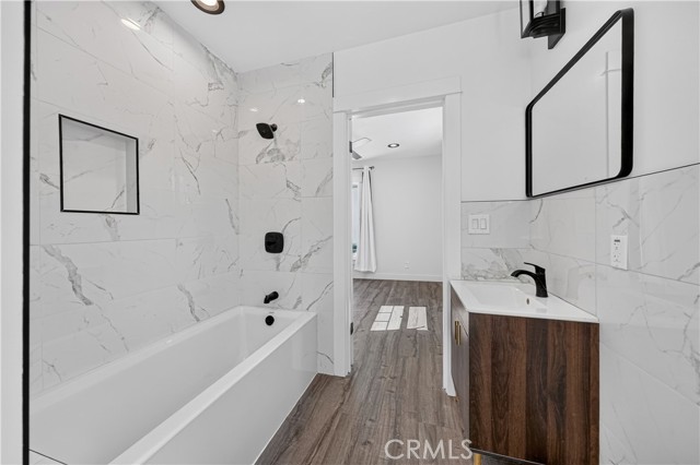 A modern bathroom featuring a white marble-look tiled wall with a recessed shower niche, a white soaking tub, and a dark wood vanity with a black faucet.
