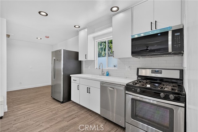 Modern white kitchen with stainless steel appliances and wood-style flooring