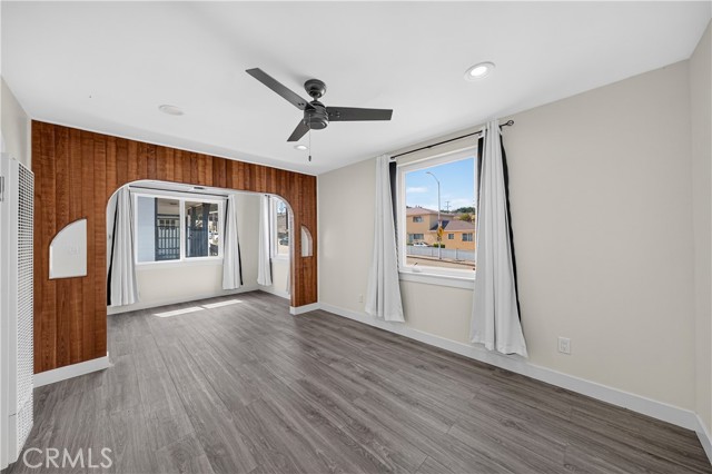 Spacious living room featuring grey wood-look flooring, a large wood-paneled archway leading to an additional space, and a ceiling fan.