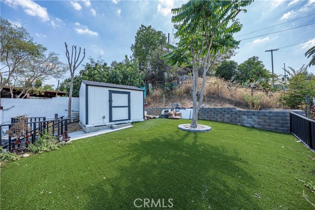 A backyard featuring artificial green grass, a storage shed, and a concrete block retaining wall.