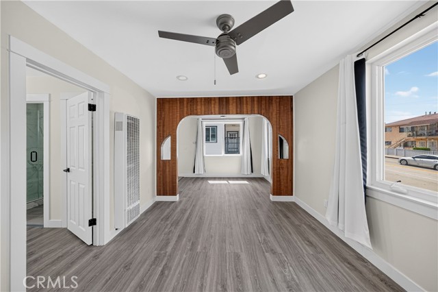 A living room with light grey wood-look flooring, white walls, and a distinctive wood-paneled archway leading to another room.