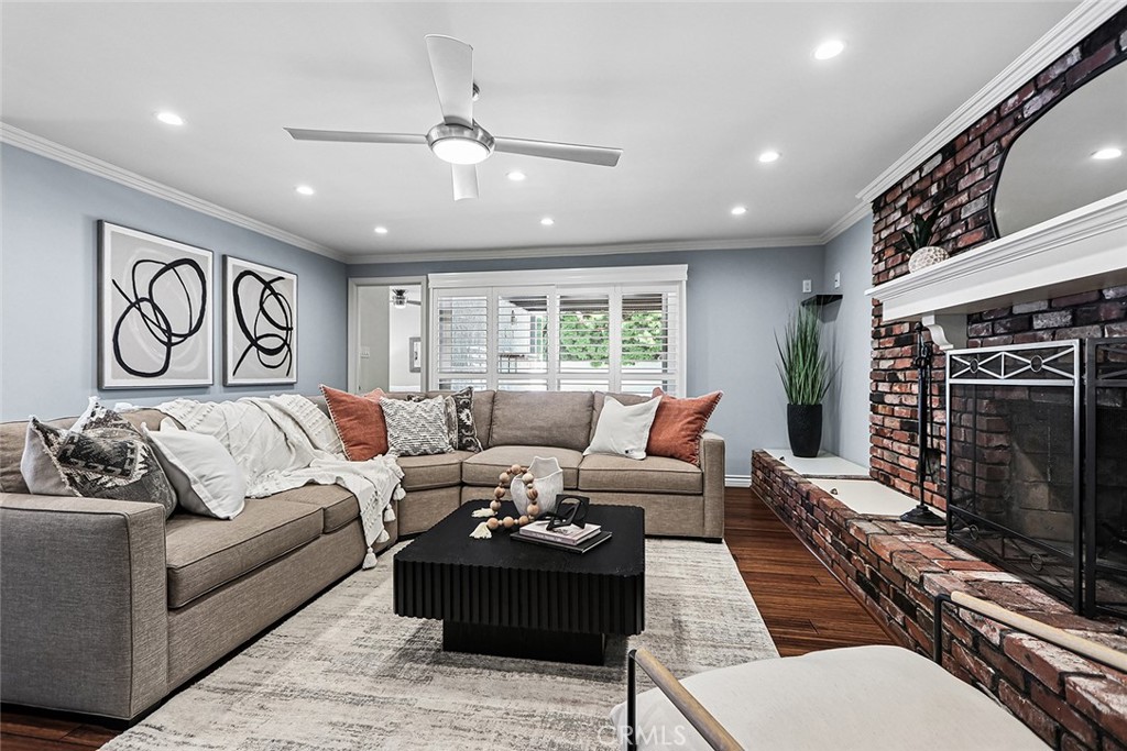 Living room at 910 Firmona Avenue with a gray sectional, brick fireplace, ceiling fan, and wide windows.