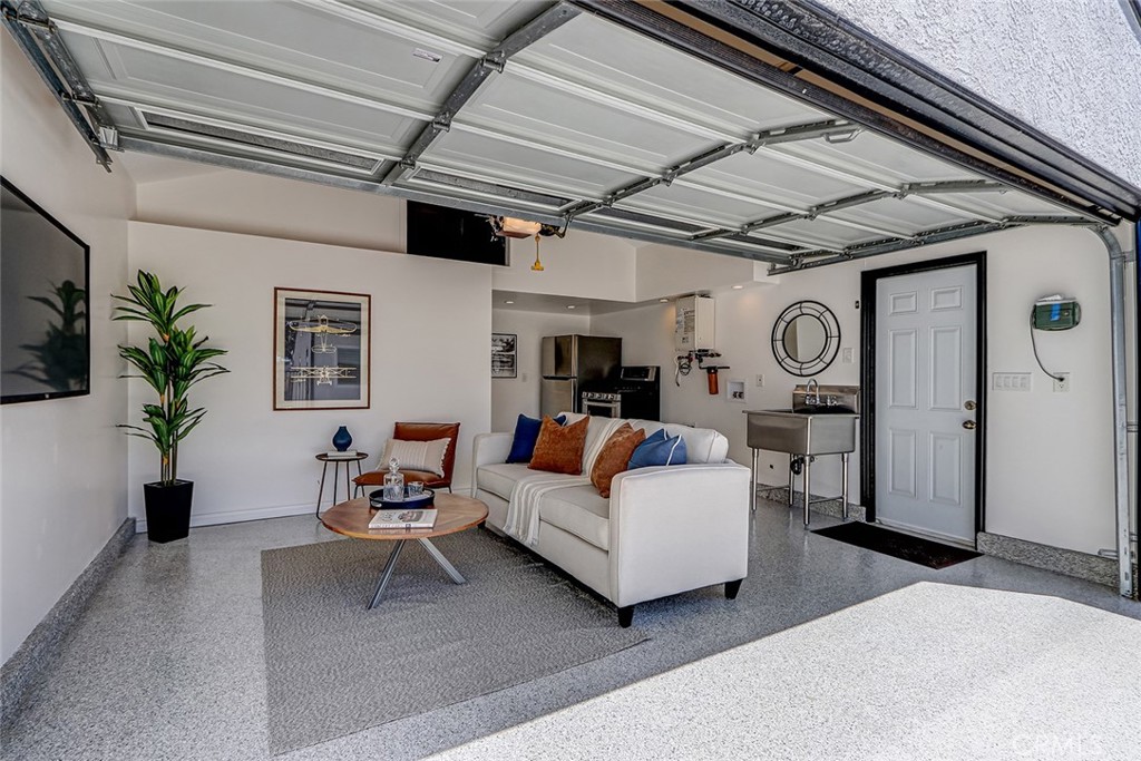 Finished garage at 910 Firmona Avenue staged as a living area, with a white sofa, coffee table, kitchenette, and open overhead garage door.