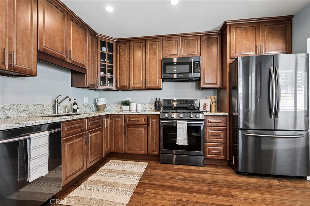 Kitchen at 910 Firmona Avenue with warm wood cabinets, granite countertops, stainless steel appliances, and hardwood floors.