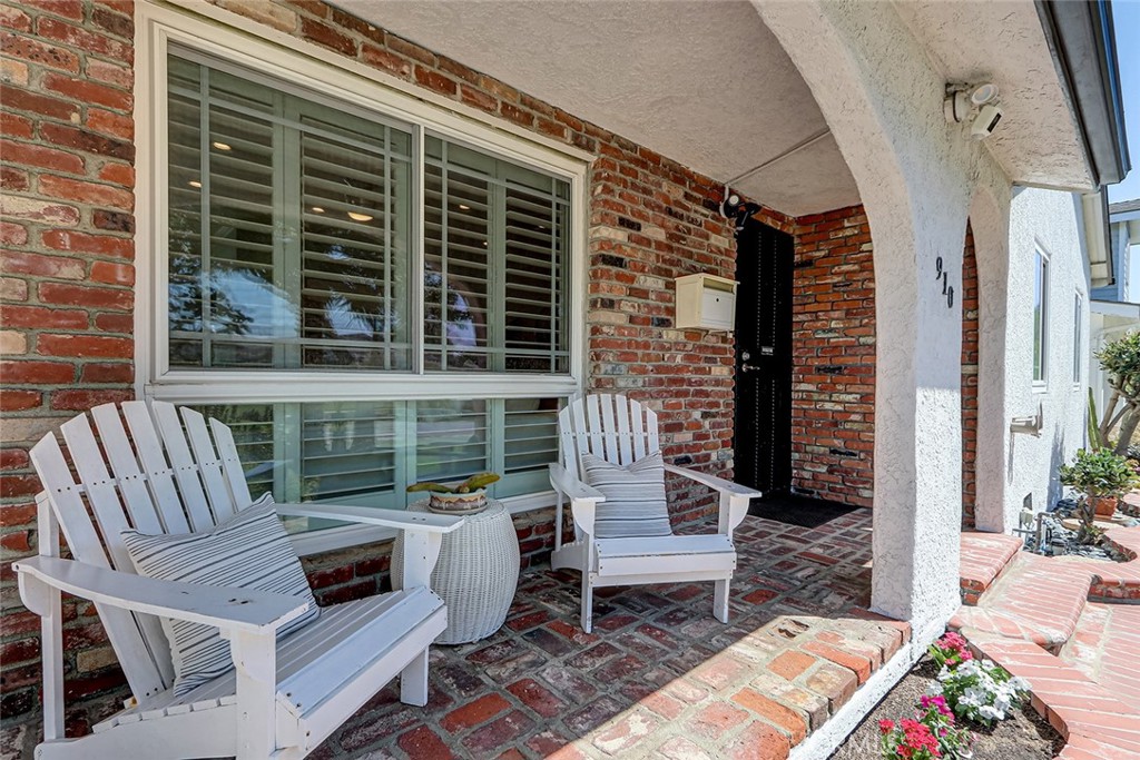 Covered brick front porch at 910 Firmona Avenue with white Adirondack chairs, a large shuttered window, and a black entry door.