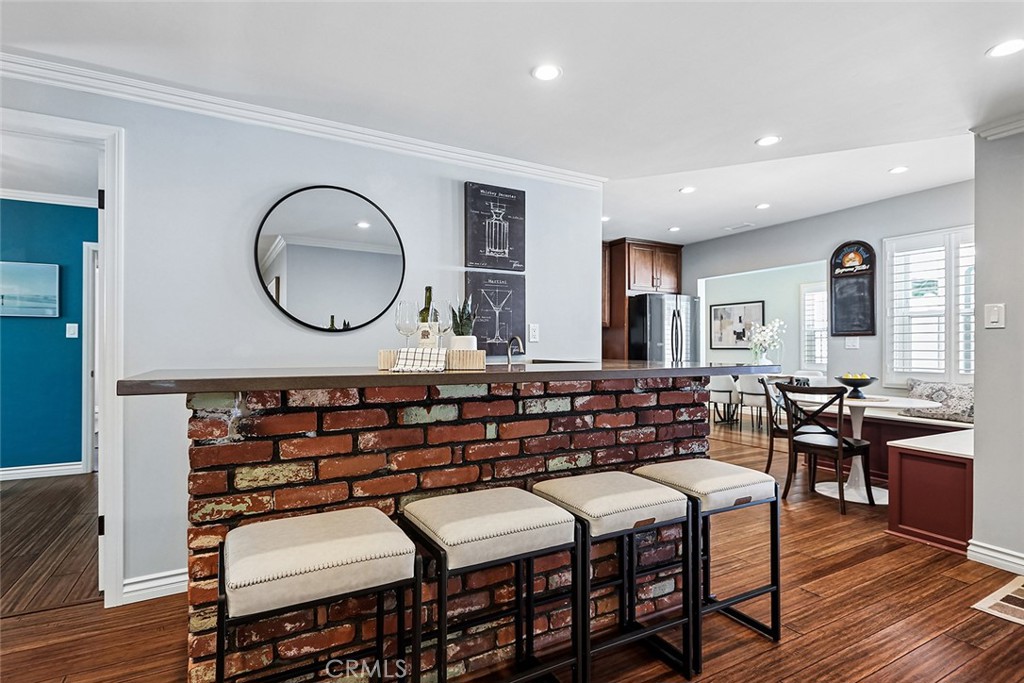 Open kitchen and dining area at 910 Firmona Avenue, with a brick-front breakfast bar, four upholstered stools, stainless steel appliances, and hardwood floors.