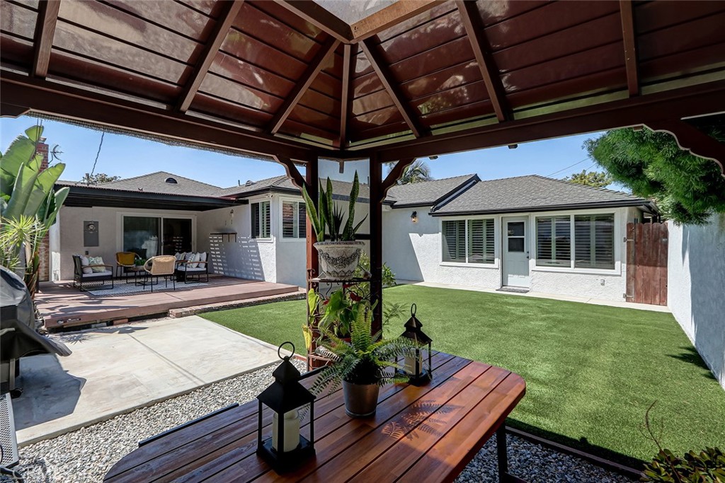 Covered wooden patio overlooking the landscaped backyard at 910 Firmona Avenue, with a lawn, gravel beds, and a white home with large windows.