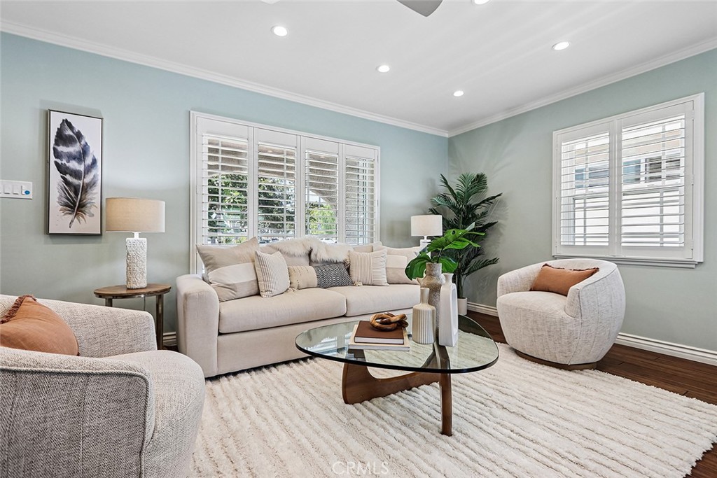Bright living room at 910 Firmona Avenue with pale blue walls, a beige sofa, two upholstered chairs, a glass coffee table, plantation shutters, and a large area rug.