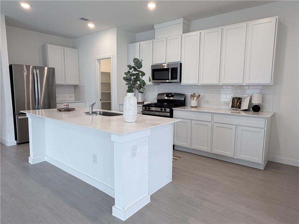 Bright white kitchen with a large island, stainless steel appliances, and gray flooring.