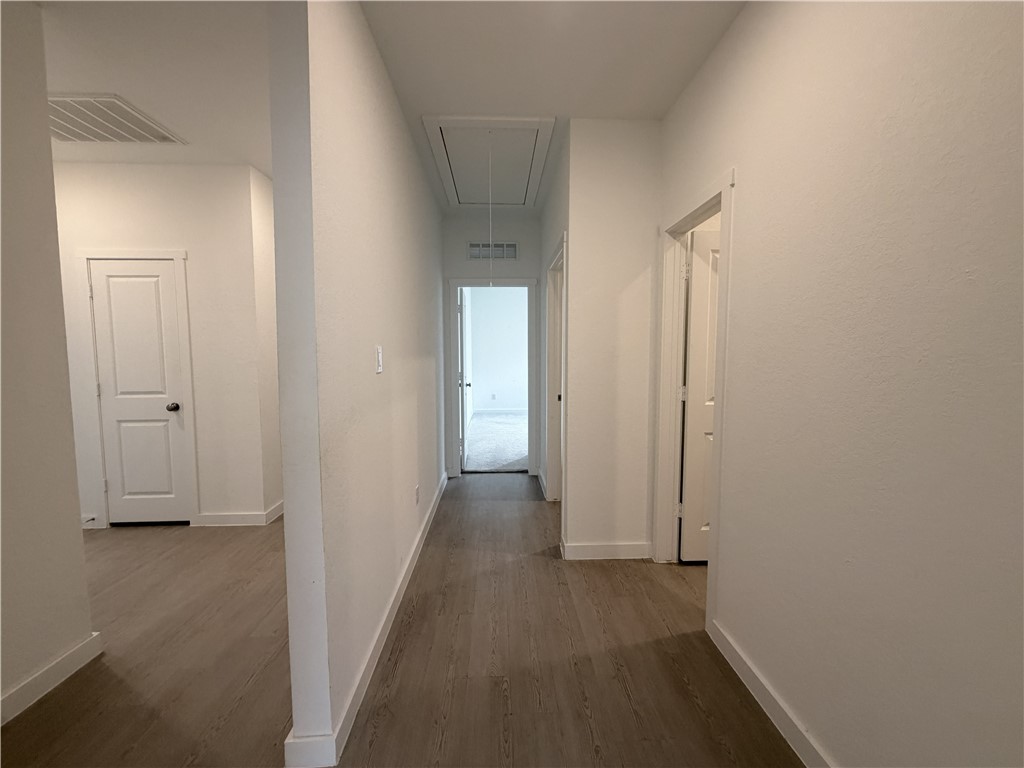 Empty hallway with wood-look flooring, white walls, and doorways to adjoining rooms.