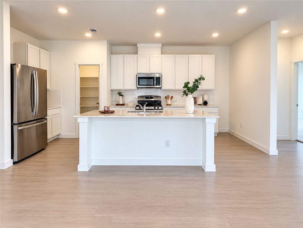 Bright kitchen with a large white island, stainless steel appliances, and light wood flooring.