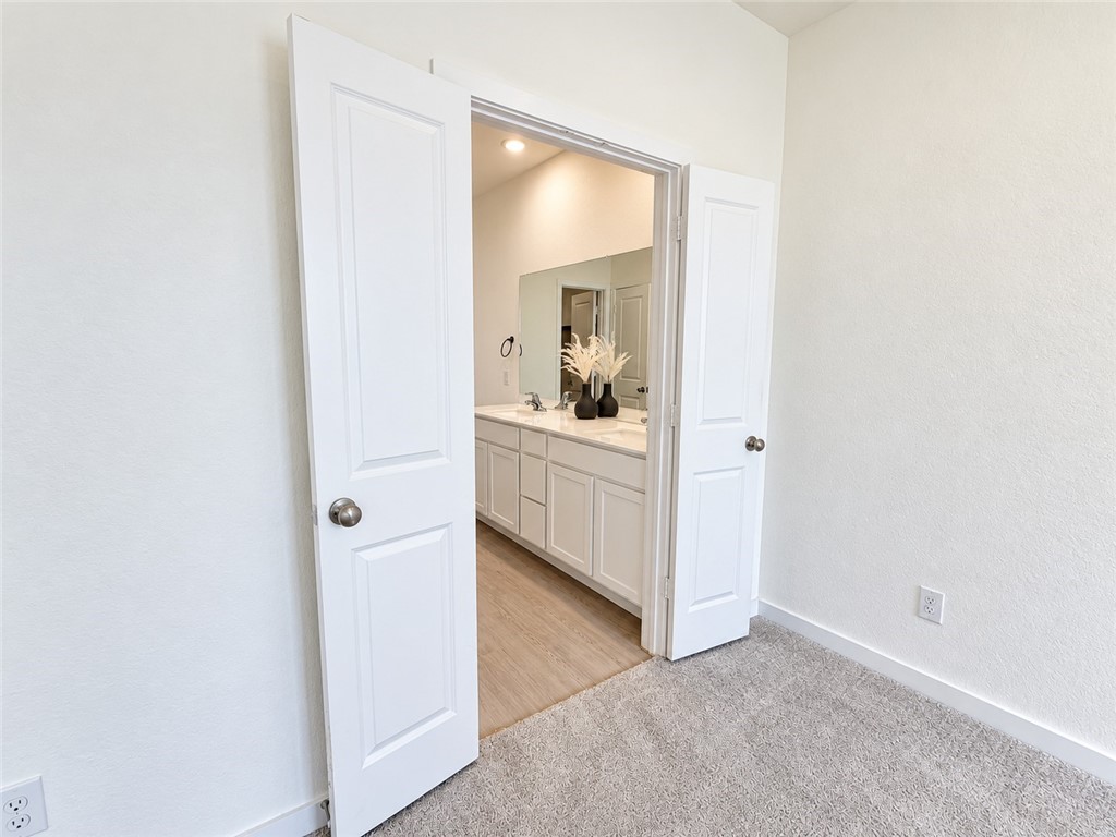 Bathroom vanity with white cabinetry and a large mirror, viewed through open double doors.