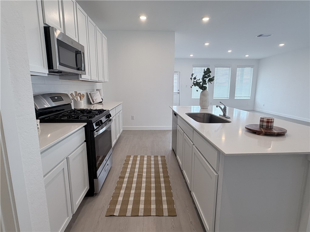White kitchen with a gas range, stainless microwave, and large island with a sink.