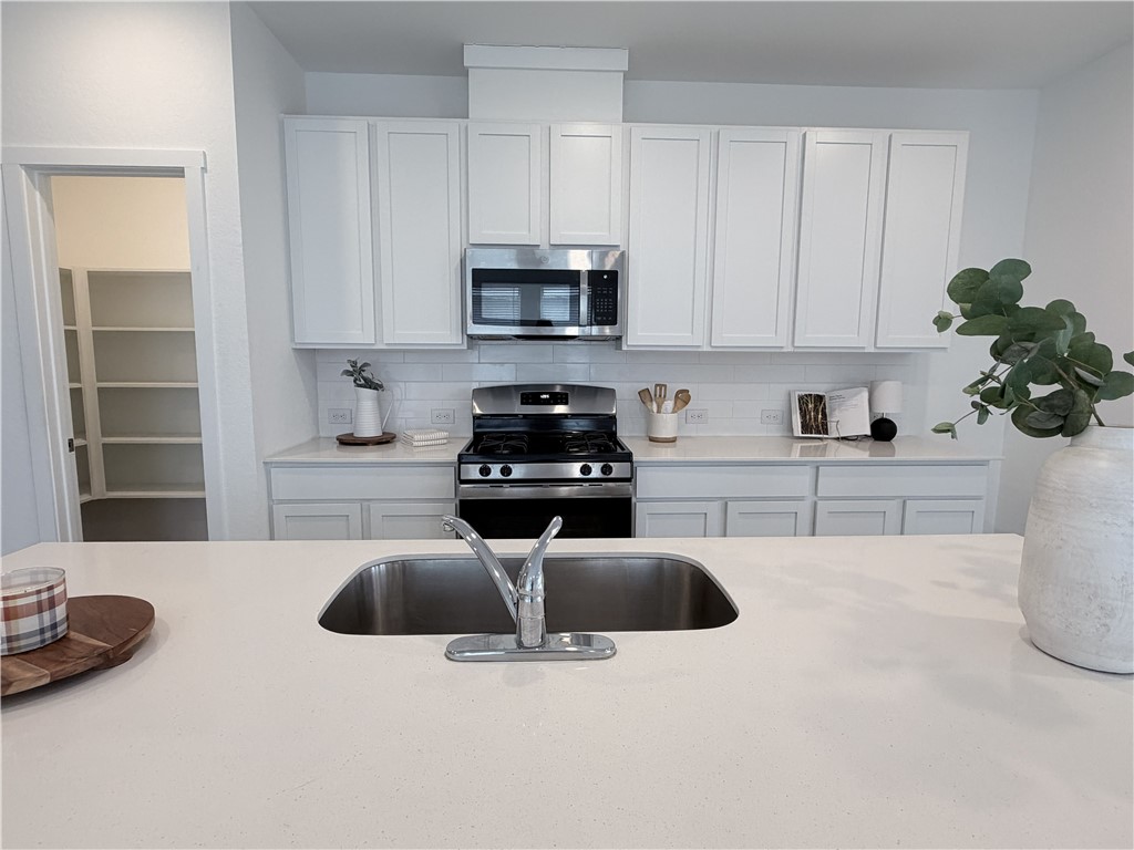 Kitchen with white cabinets, stainless steel range, and a large island sink.