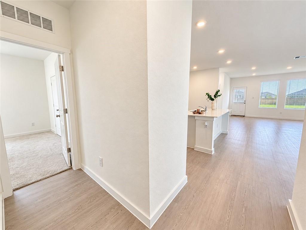 Open living area with wood-look floors, kitchen island, and an adjoining carpeted room.