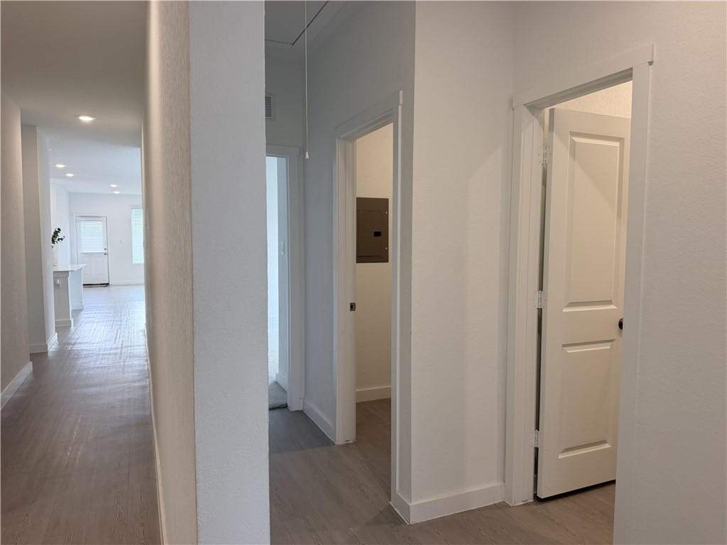 Interior hallway with gray wood-look floors, several doorways, and a bright room at the end.