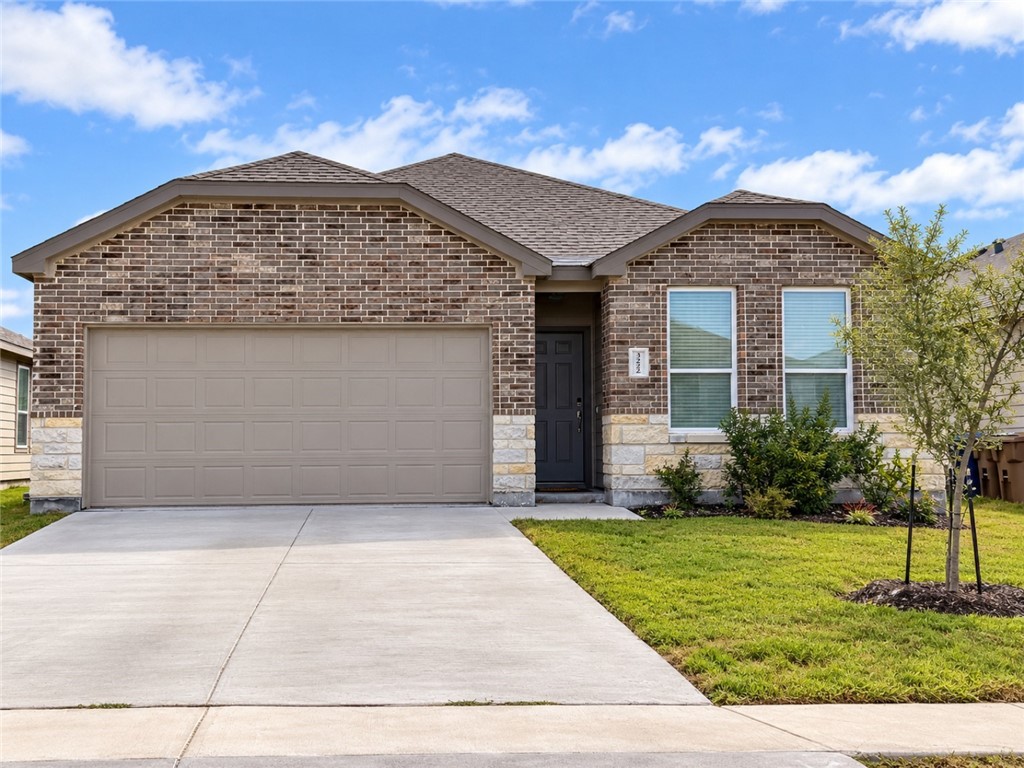 Brick house with a two-car garage, wide concrete driveway, and front lawn.