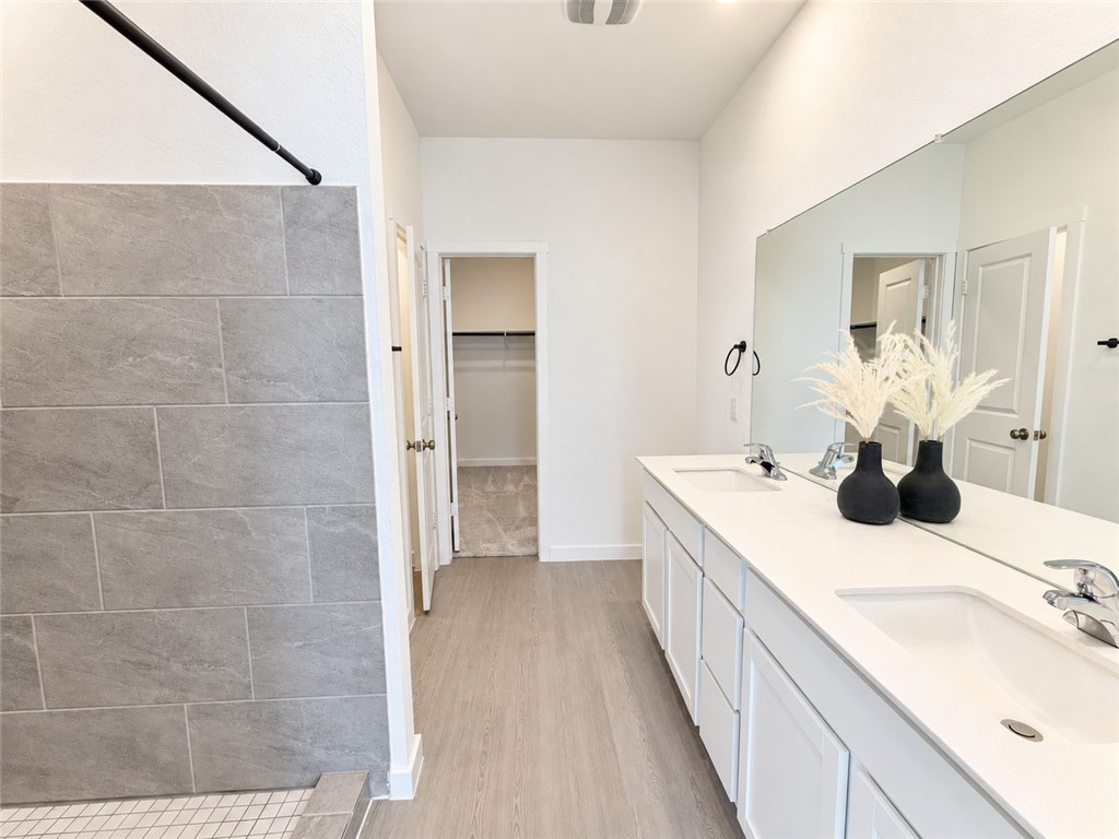 Bathroom with a long double vanity, large mirror, and gray tiled shower wall.