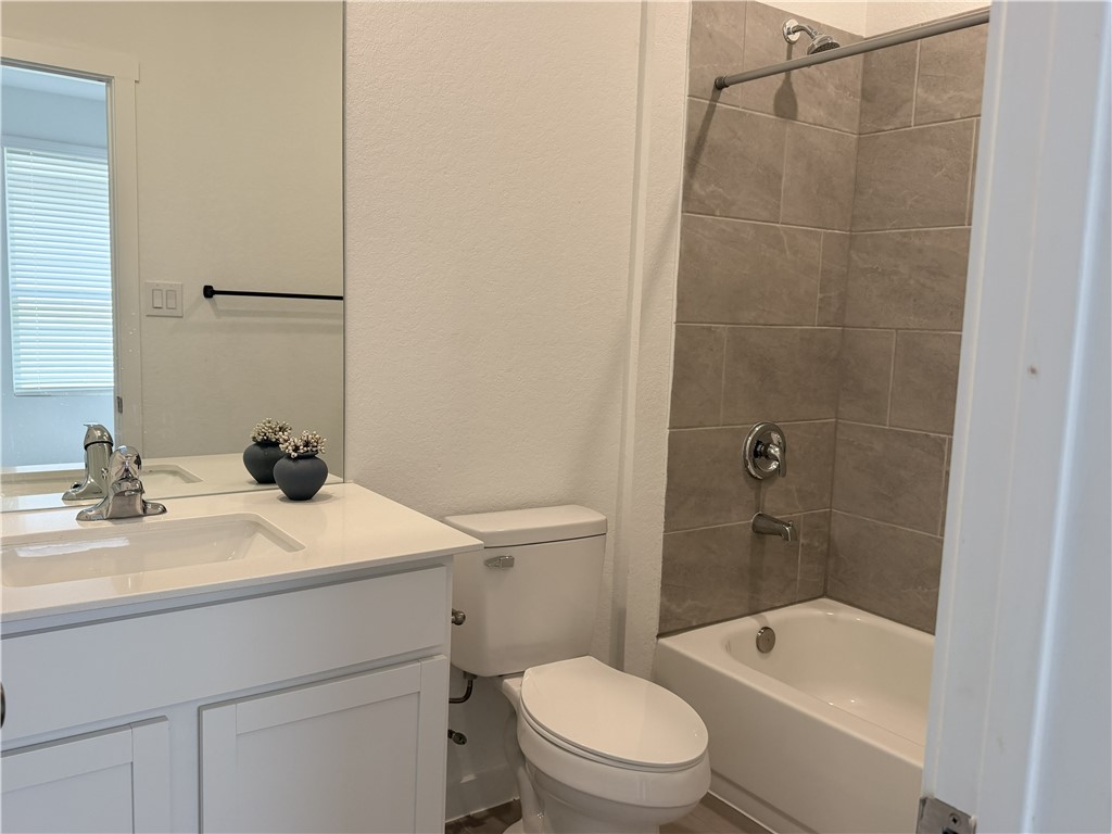Bathroom with a white vanity, toilet, and tub-shower lined with taupe tile.