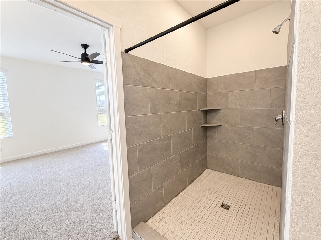 Walk-in tiled shower with corner shelves beside a carpeted bedroom.