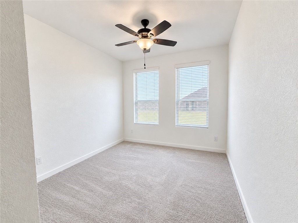Vacant carpeted room with two windows and a ceiling fan.