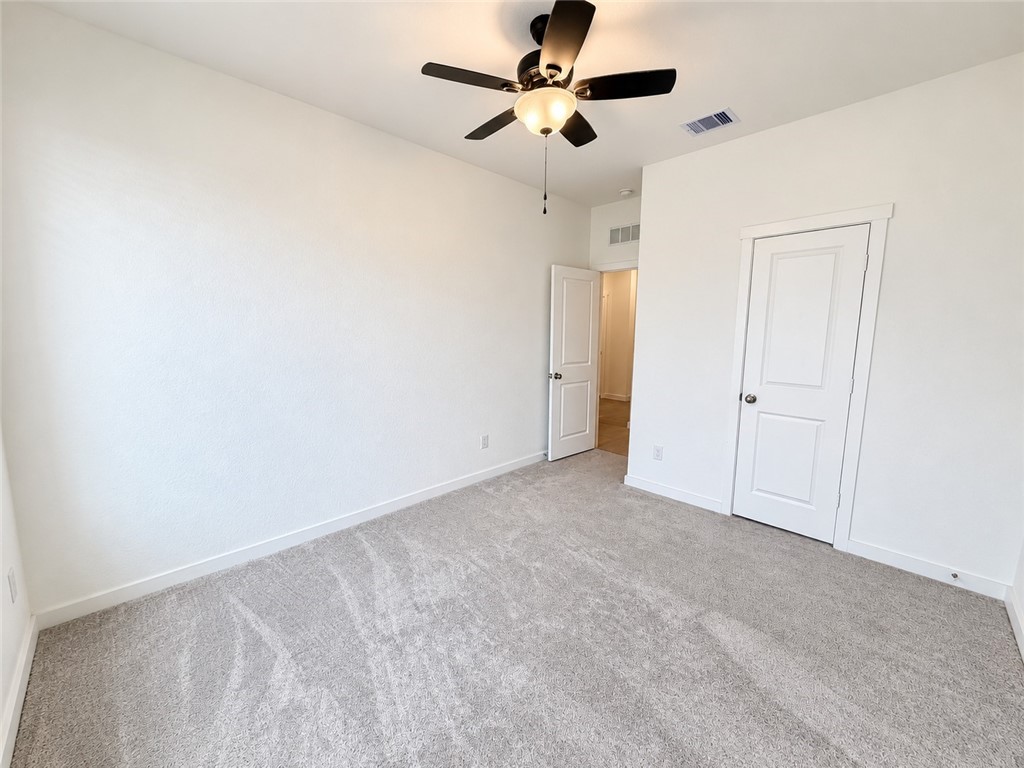 Empty carpeted bedroom with a ceiling fan and two white doors.