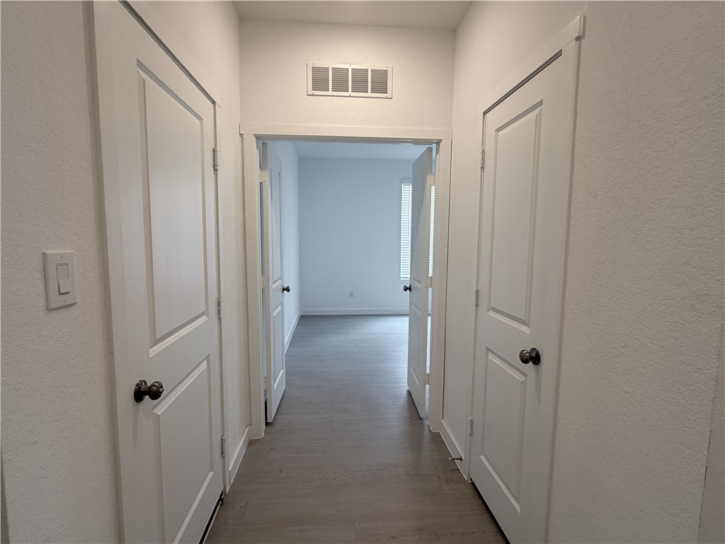 Hallway with white doors and gray plank flooring leading to a bright, empty room.