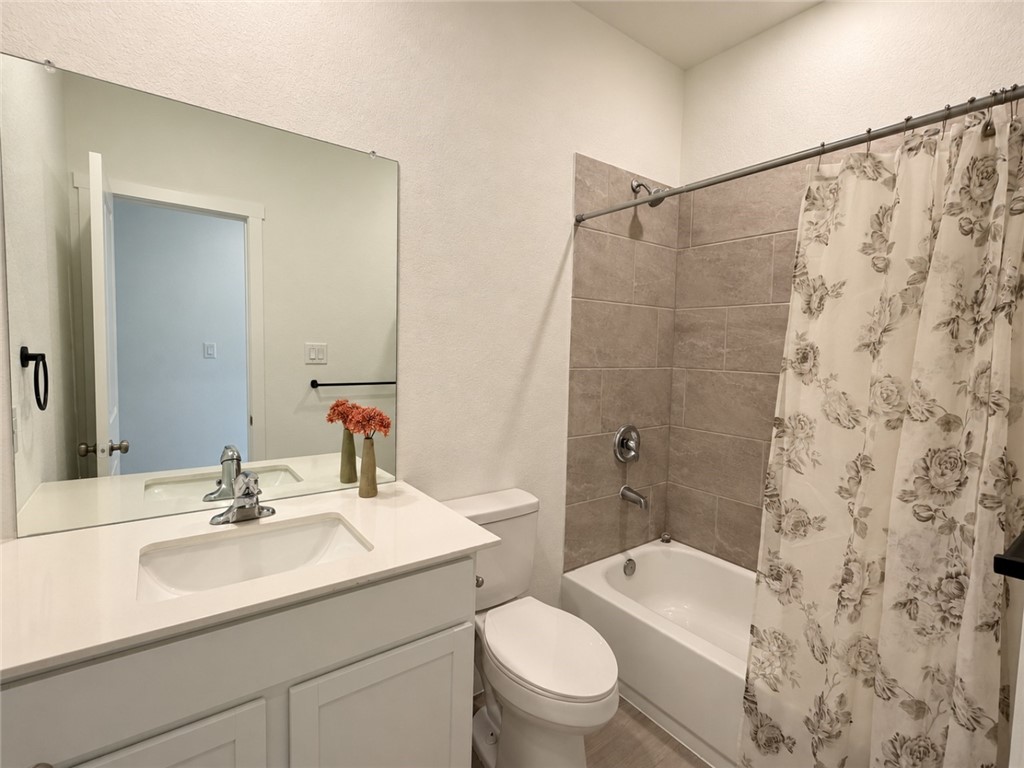 Bathroom with a white vanity, large mirror, and tub behind a floral shower curtain.