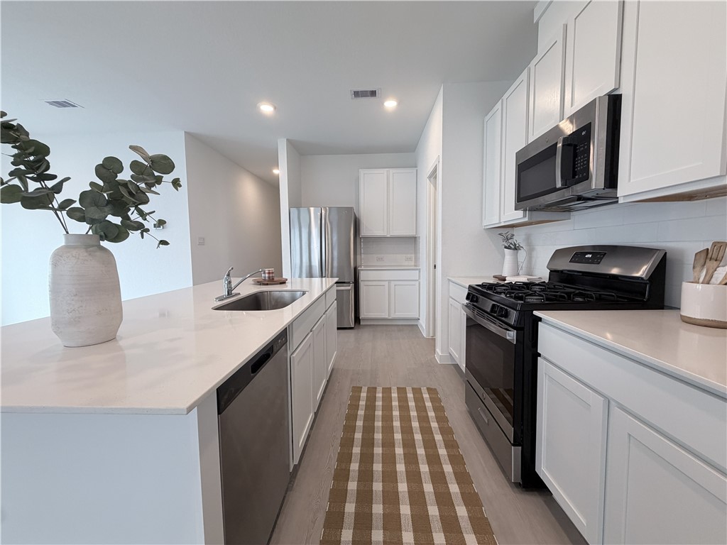 Bright kitchen with white cabinetry, stainless appliances, and a long island with sink.