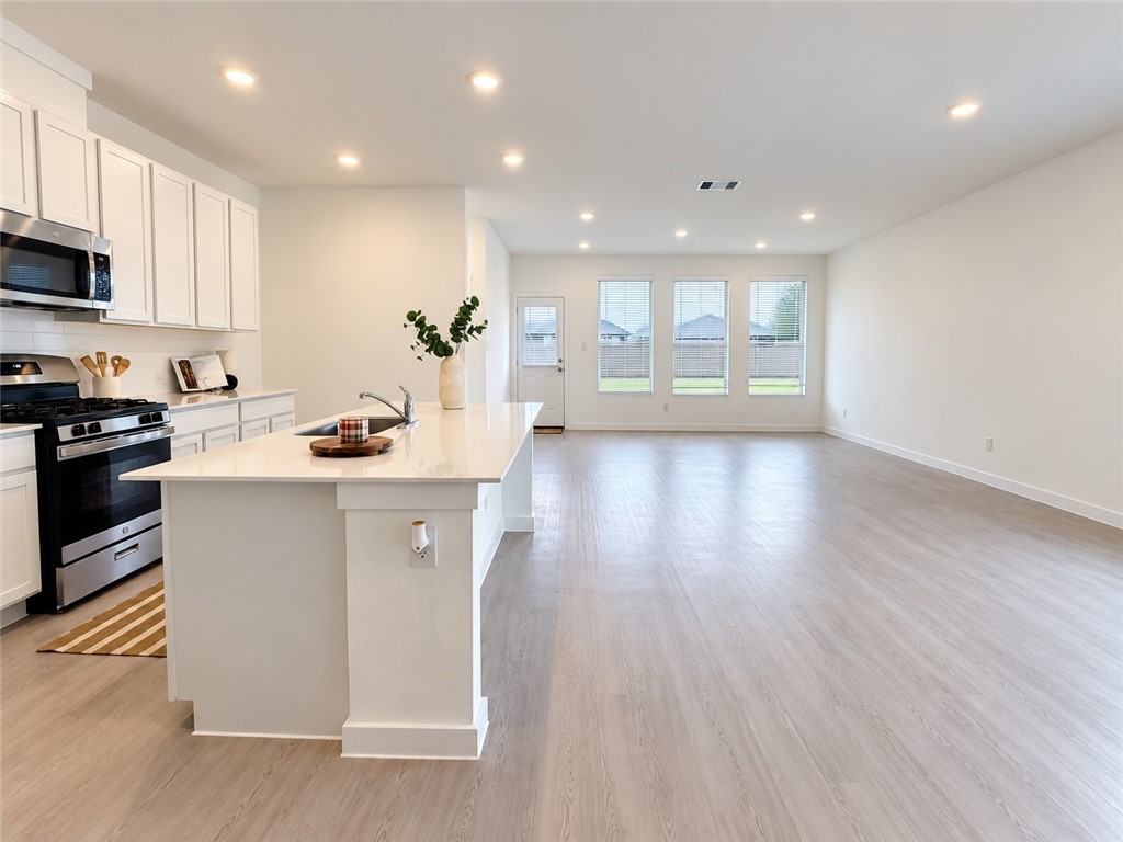 Open kitchen and living area with a large island, white cabinetry, and windows along the back wall.