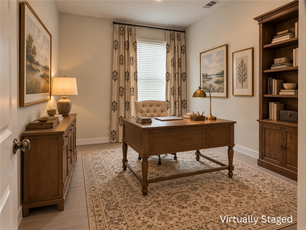 Virtually staged home office with a wooden desk, built-in shelving, and patterned rug.