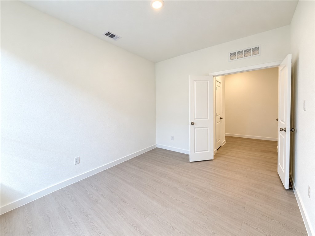 Empty room with light wood-look flooring and open double doors to a hallway.
