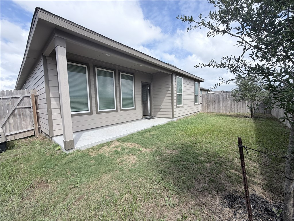 Rear exterior of a gray home with a covered patio and fenced grassy yard.